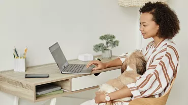 Persona al computer con un cane in braccio.