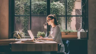 Persona al computer vicino a una finestra con piante.