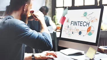 Persona lavora al computer con schermo che mostra 'FINTECH'.