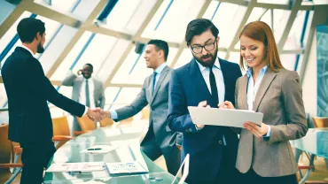 Gruppo di persone in una riunione aziendale, due si stringono la mano.