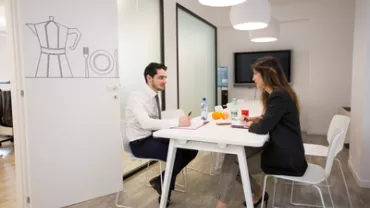 Due persone in riunione sedute a un tavolo bianco in ufficio moderno.