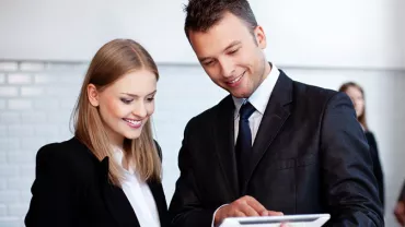 Due persone in abiti eleganti guardano un tablet con interesse.