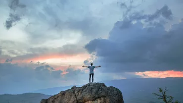 Persona su una roccia con le braccia aperte verso il cielo al tramonto.