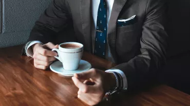 Persona in abito tiene una tazza di caffè su tavolo di legno.