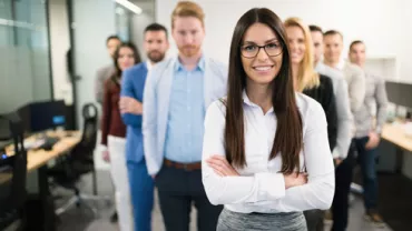 Gruppo di persone in ufficio, persona in primo piano con occhiali sorridente.