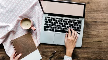 Persona usa un laptop con una tazza di caffè e un libro su tavolo di legno.